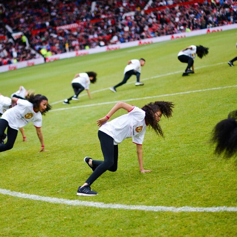 A photo of a group of children dancing in the centre circle of Old Trafford football stadium, Manchester at our Red Heart United event in 2015